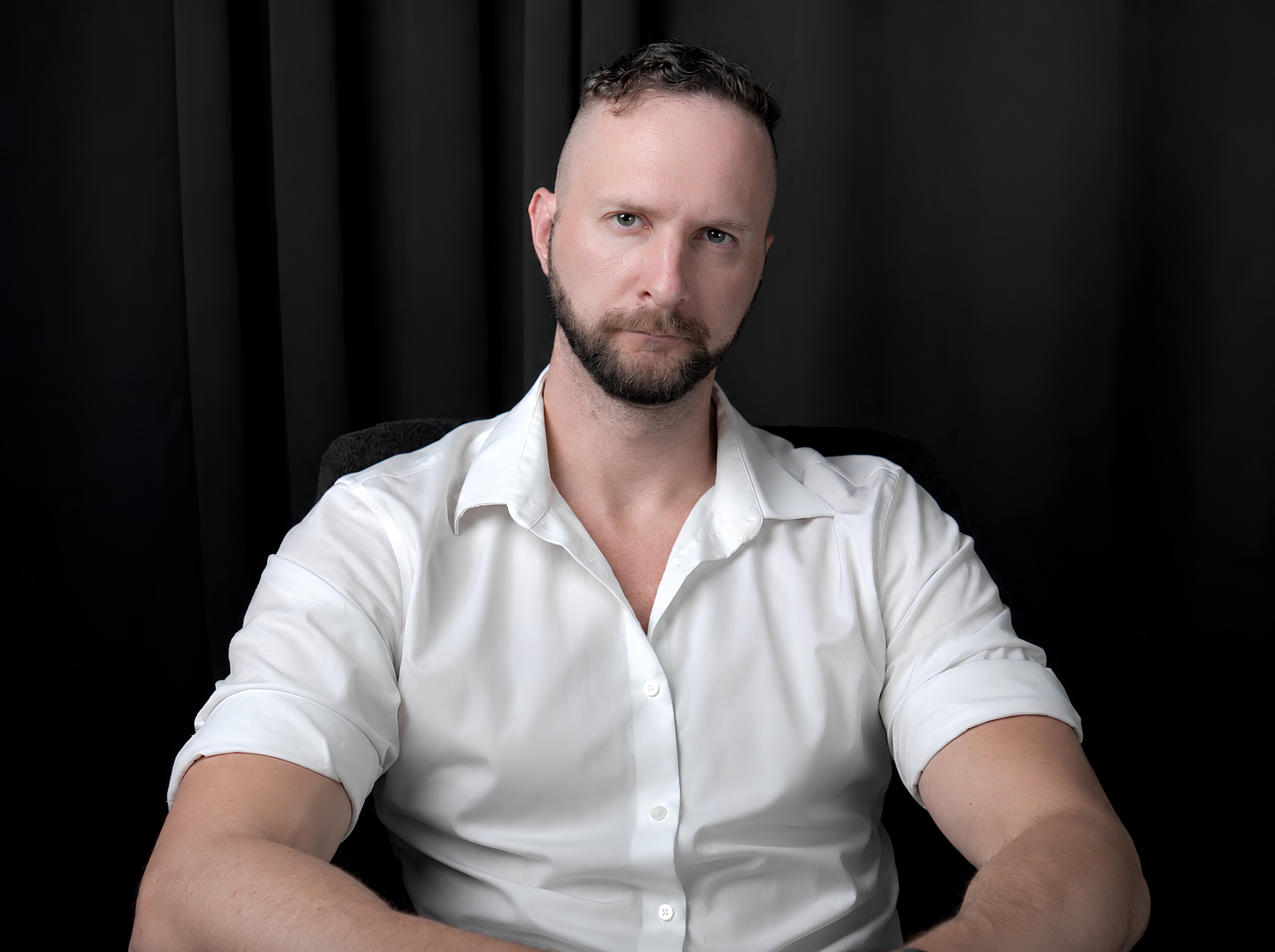 Aleks Markov seated in a white shirt against a dark backdrop